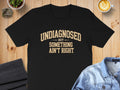 Black t-shirt with tan text reading "UNDIAGNOSED BUT SOMETHING AIN'T RIGHT."