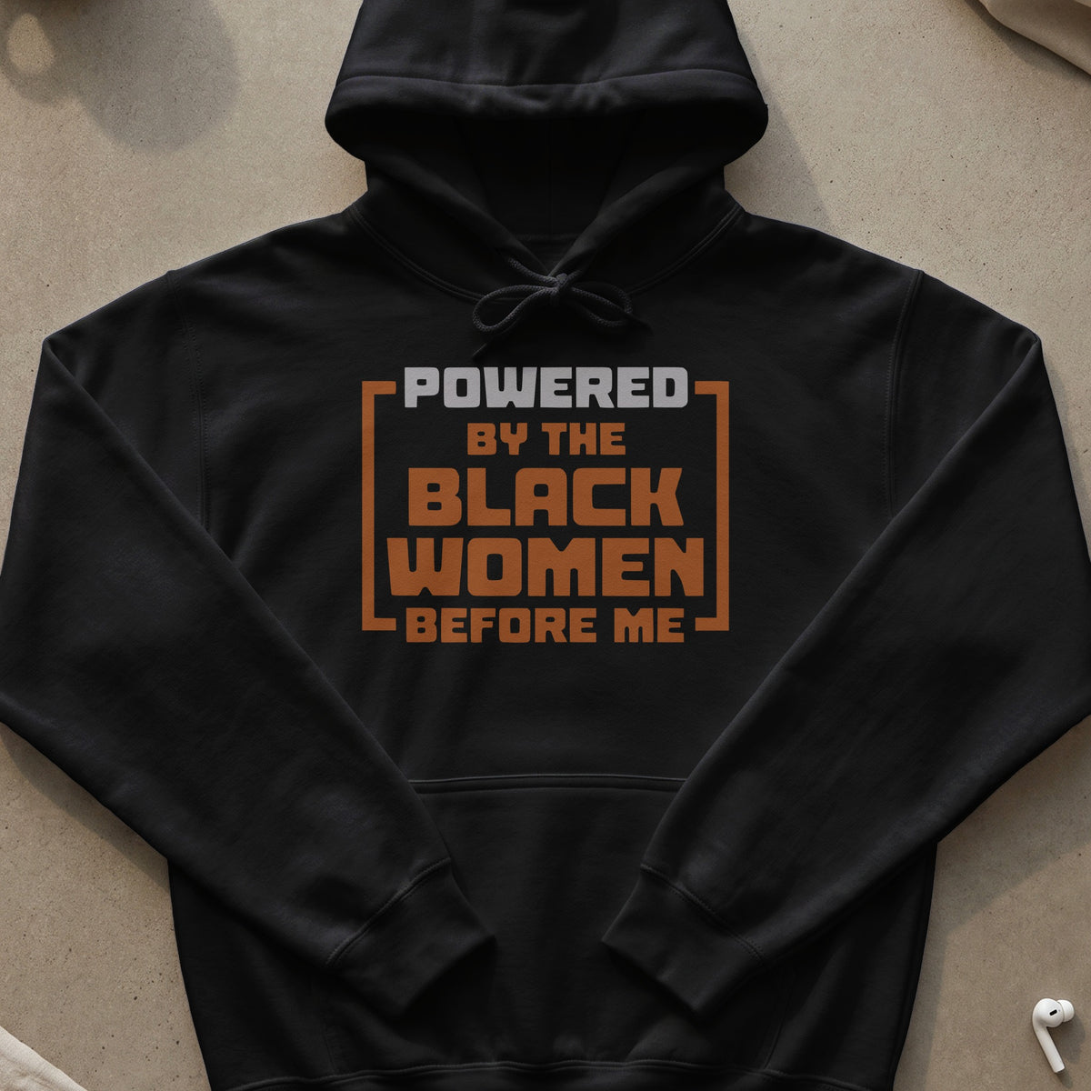 Black hoodie with "POWERED BY THE BLACK WOMEN BEFORE ME" text in orange and grey.