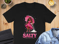 Black t-shirt with illustration of woman holding umbrella, pouring salt, with text "DON'T BE SALTY".