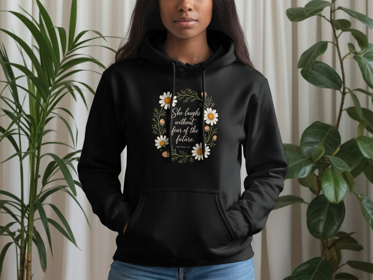 Black hoodie with floral wreath graphic and "She laughs without fear of the future. PROVERBS 31:25" text.