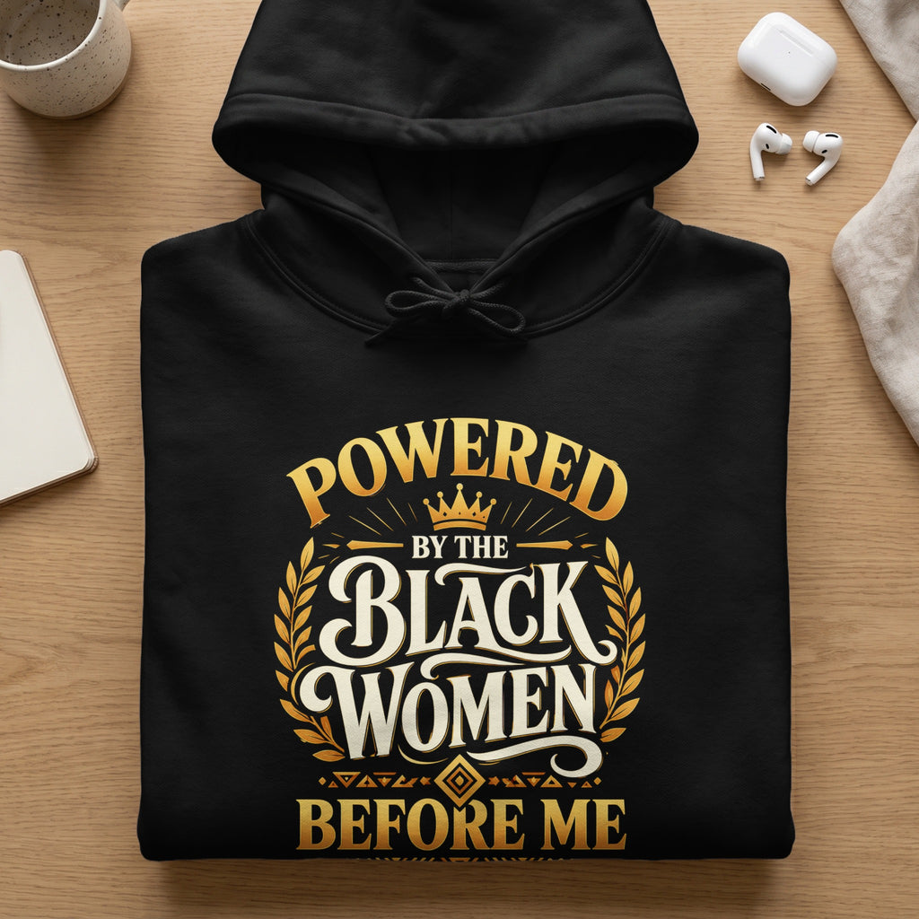 Black hoodie with "POWERED BY THE BLACK WOMEN BEFORE ME" graphic in gold.