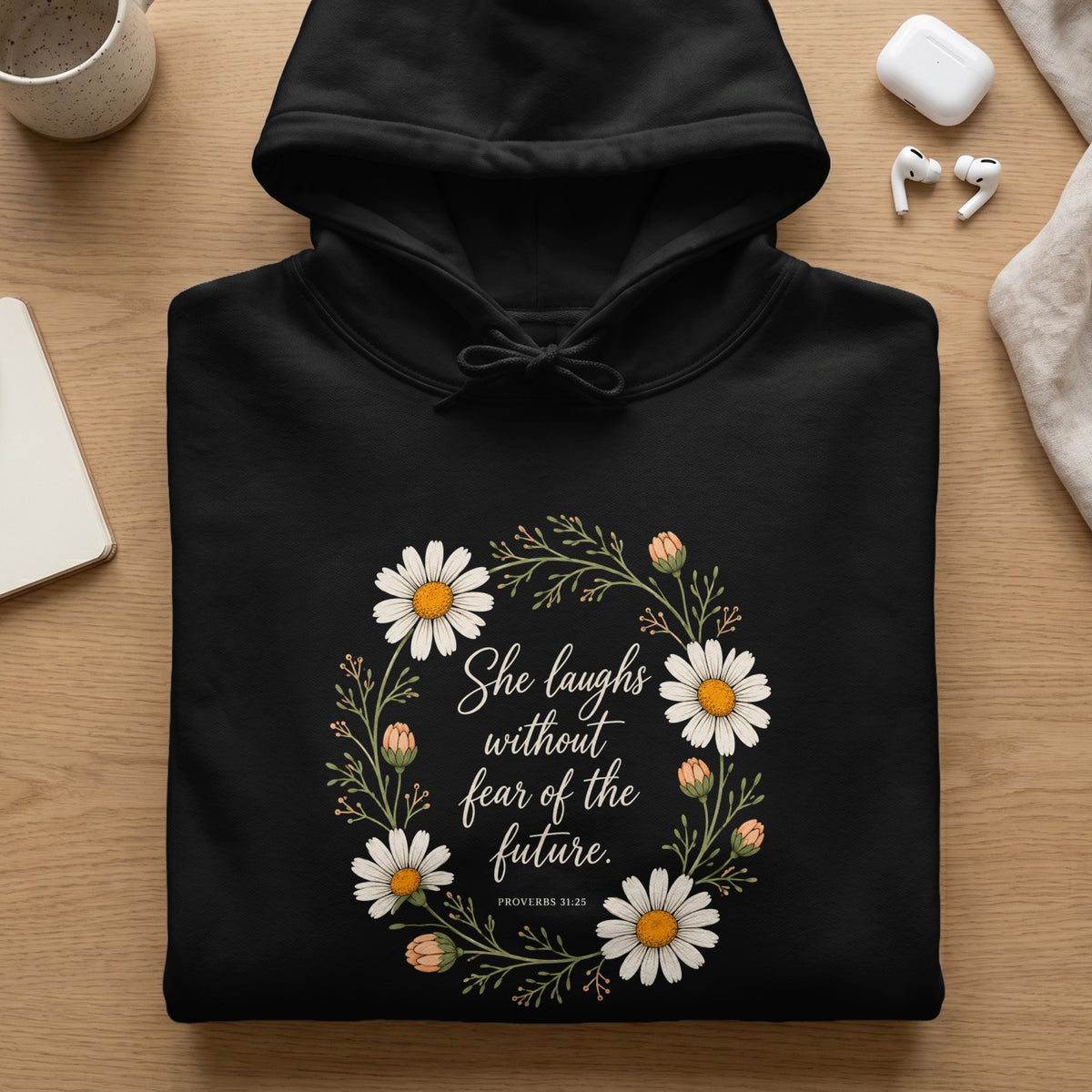 Black hoodie with floral wreath and text "She laughs without fear of the future."