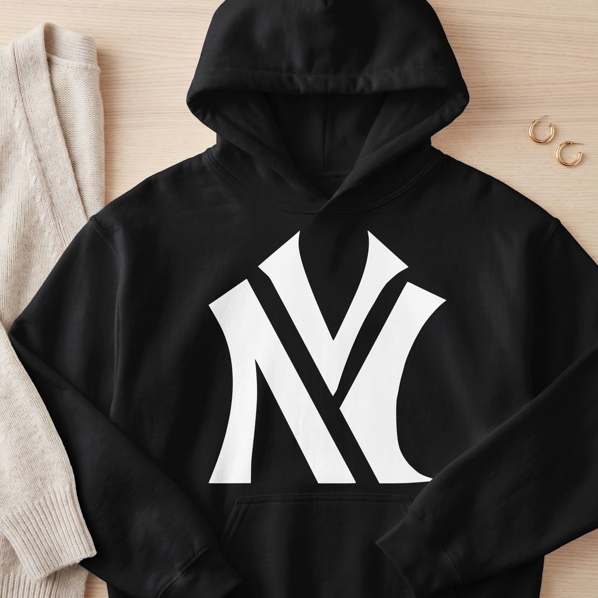 Black hoodie with white stylized "NY" logo on chest, next to beige sweater.