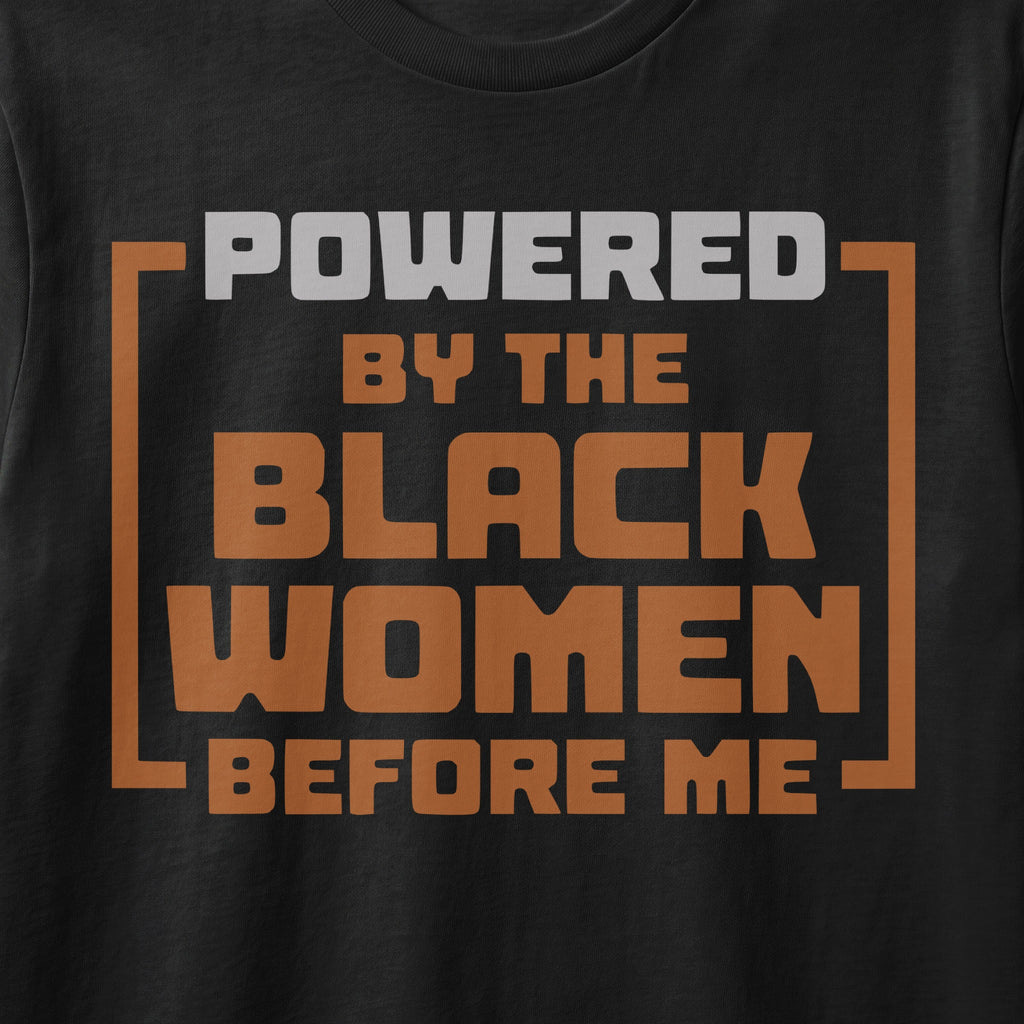 Black t-shirt with "POWERED BY THE BLACK WOMEN BEFORE ME" text in gray and orange.