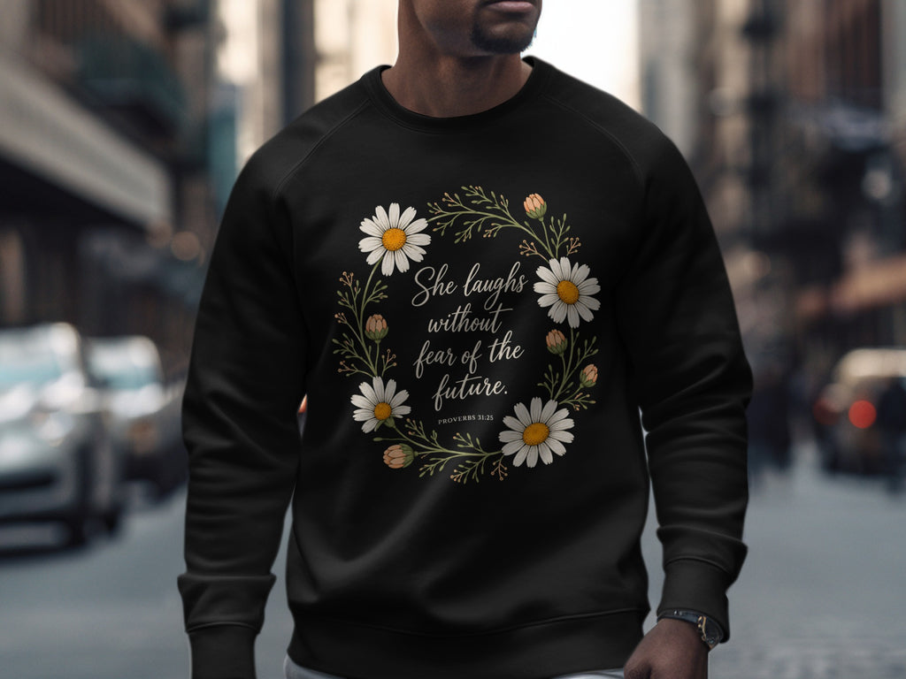 Black sweatshirt with floral wreath and text "She laughs without fear of the future. PROVERBS 31:25."