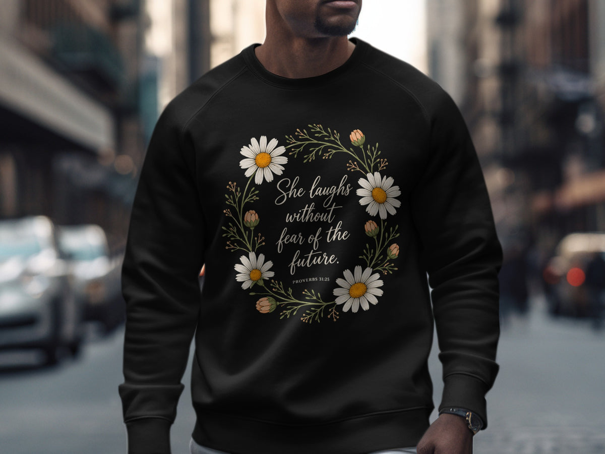 Black sweatshirt with floral wreath and text "She laughs without fear of the future. PROVERBS 31:25."