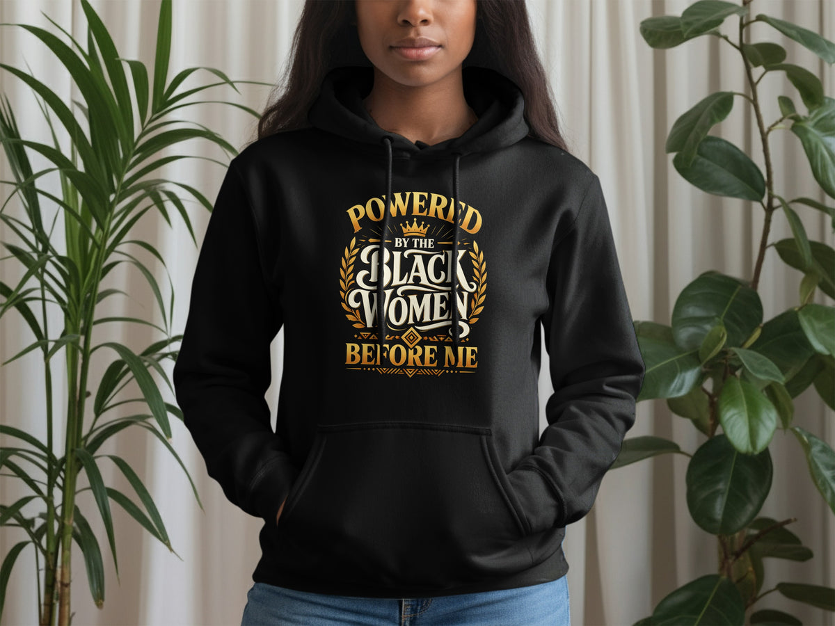 Black hoodie with gold text reading "Powered by the Black Women Before Me".