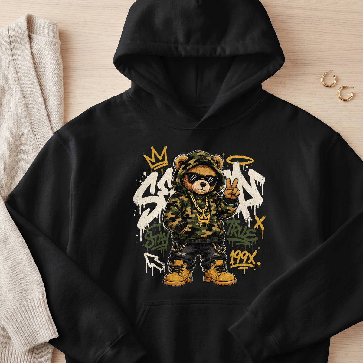 Black hoodie with graphic of a hip-hop teddy bear wearing sunglasses, gold chain, and camouflage.